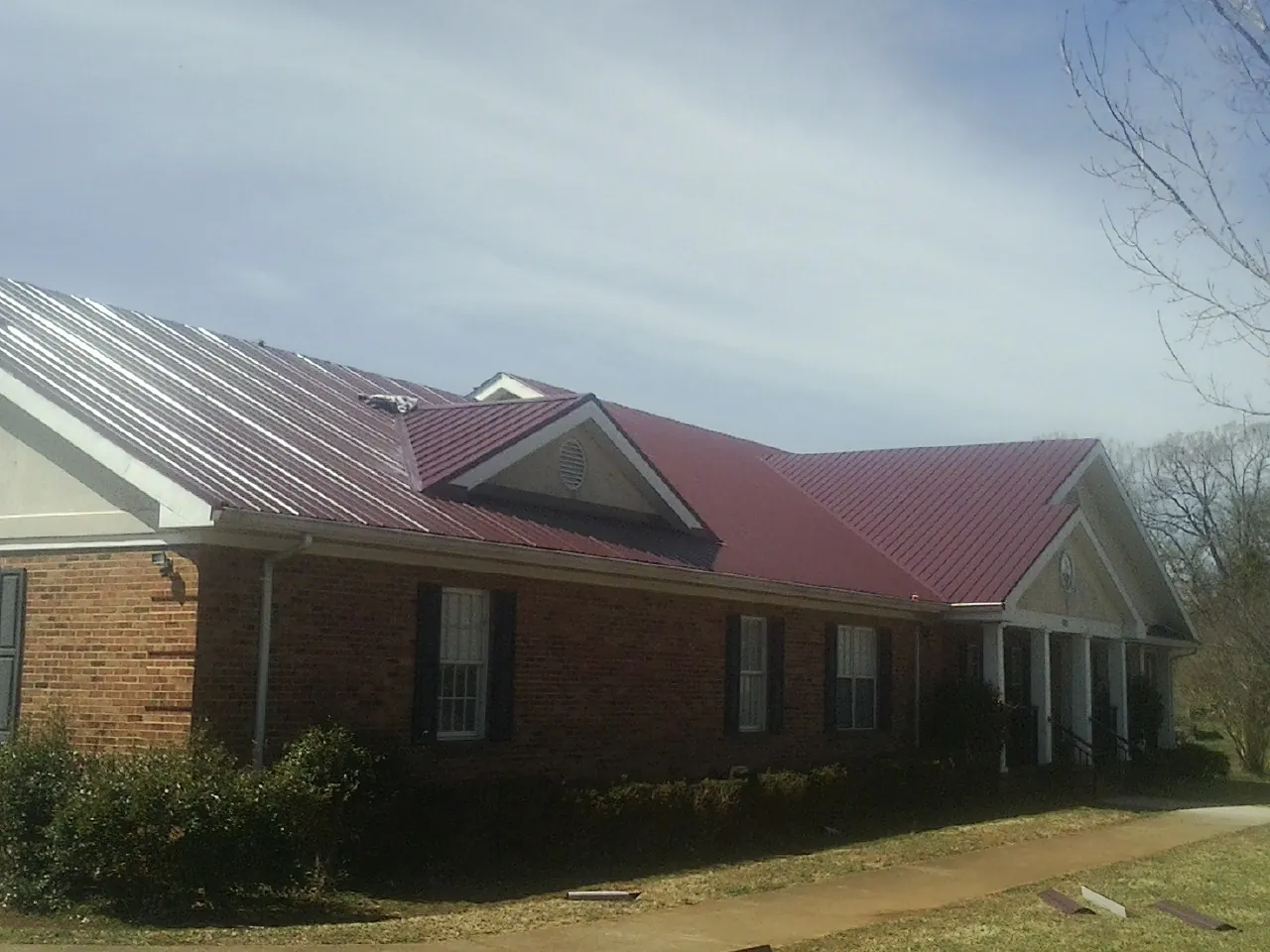 Red metal roof with gabled entries on a long brick building, from a Hail Damage Roof Repair job in Sprague River