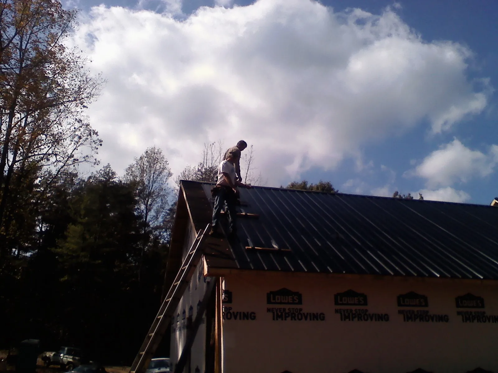 Roofer fastening dark metal panels high against a cloudy sky, from a Roof Inspection job in Sprague River