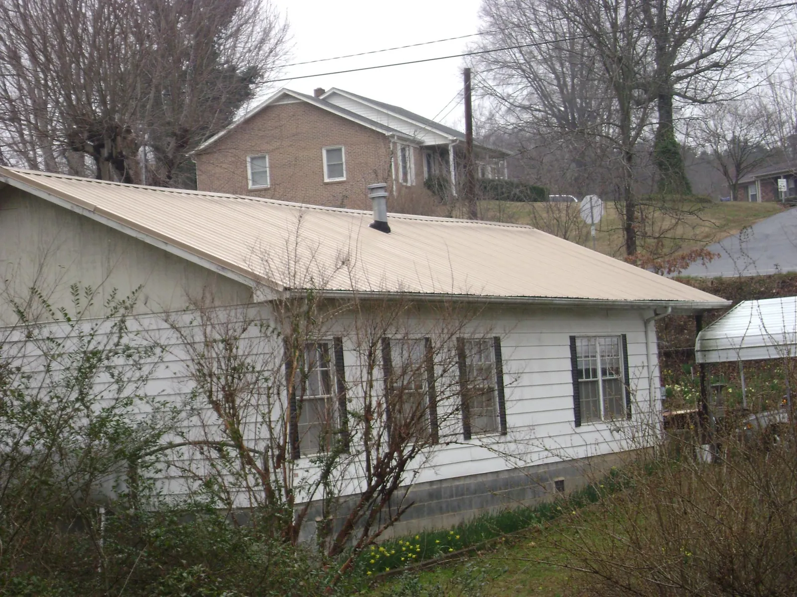 Tan metal roof on a white sided house set into a hillside — Commercial Roofing by Roofing Brothers in Sprague River